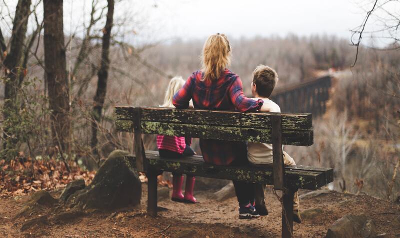 mother and two children sitting on wooden bench in nature
